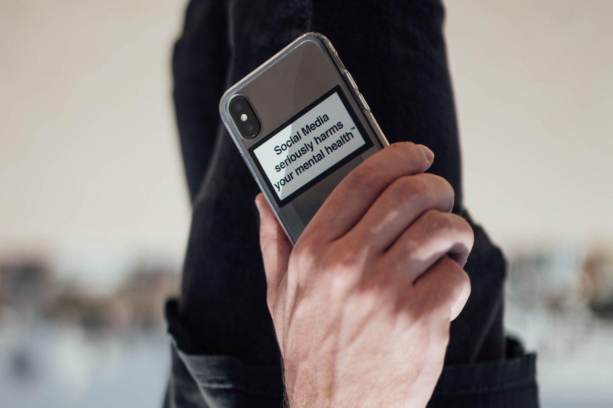 Homem a segurar num smartphone com um autocolante onde se lê "Social Media seriously harms your mental health"