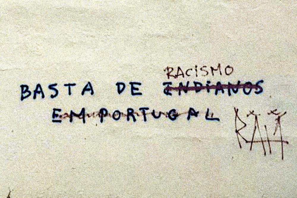 Fotografia de uma parede grafitada, na Amadora, onde se lê Basta de Racismo depois de visivelmente, alguém ter adulterado um grafiti originalmente racista.