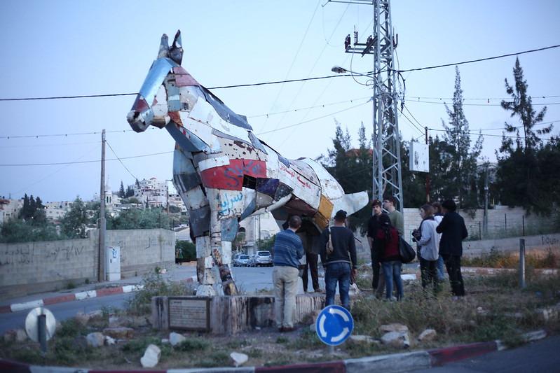 O Cavalo de Jenin, a escultura de um cavalo feito de pedaços de diversos materiais rodeado por um grupo de jovens, provavelmente no campo de Jenin