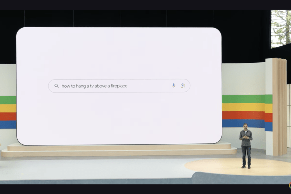 Imagem da Google I/O com Sundar Pichai, CEO da Google, perto de um gigante ecrã demonstrando o AI Overview