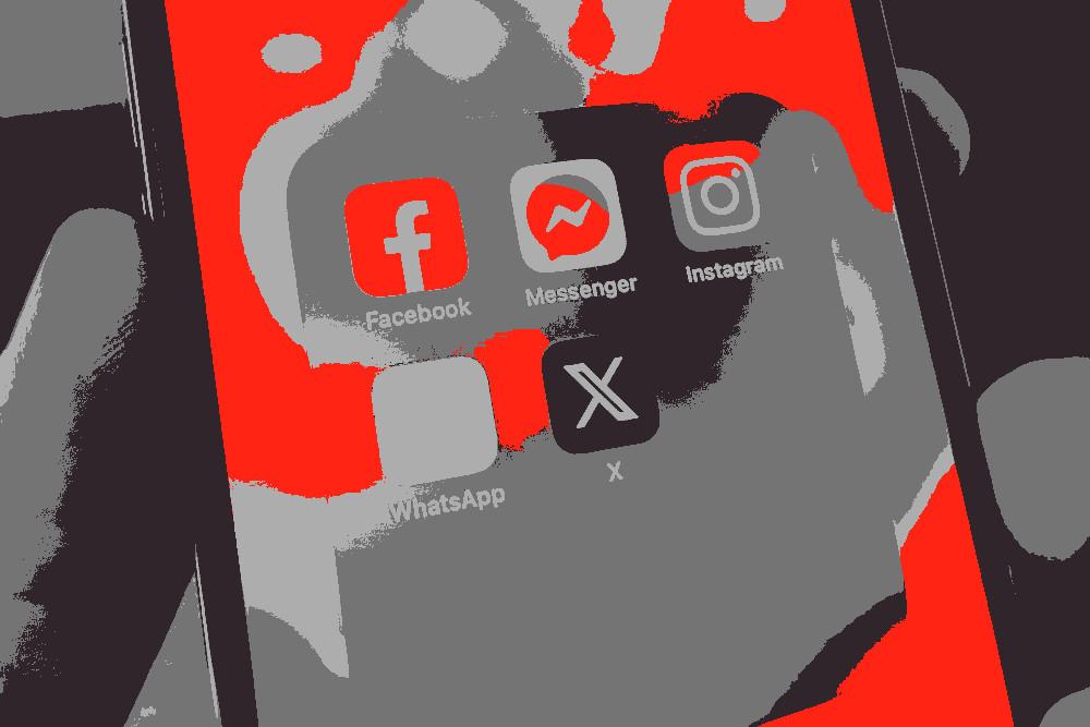 Imagem ilustrativa onde se vê uma mão a segurar num iPhone na pasta de apps de social media.