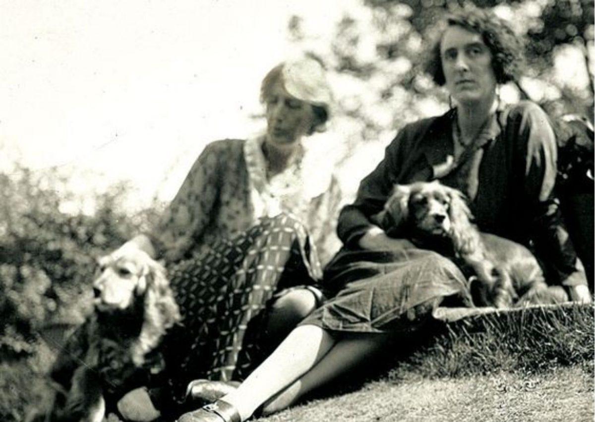 Virginia Woolf e Vita Sackville-West com os seus cães, sentadas na relva. Ambas vestem vestidos longos. 