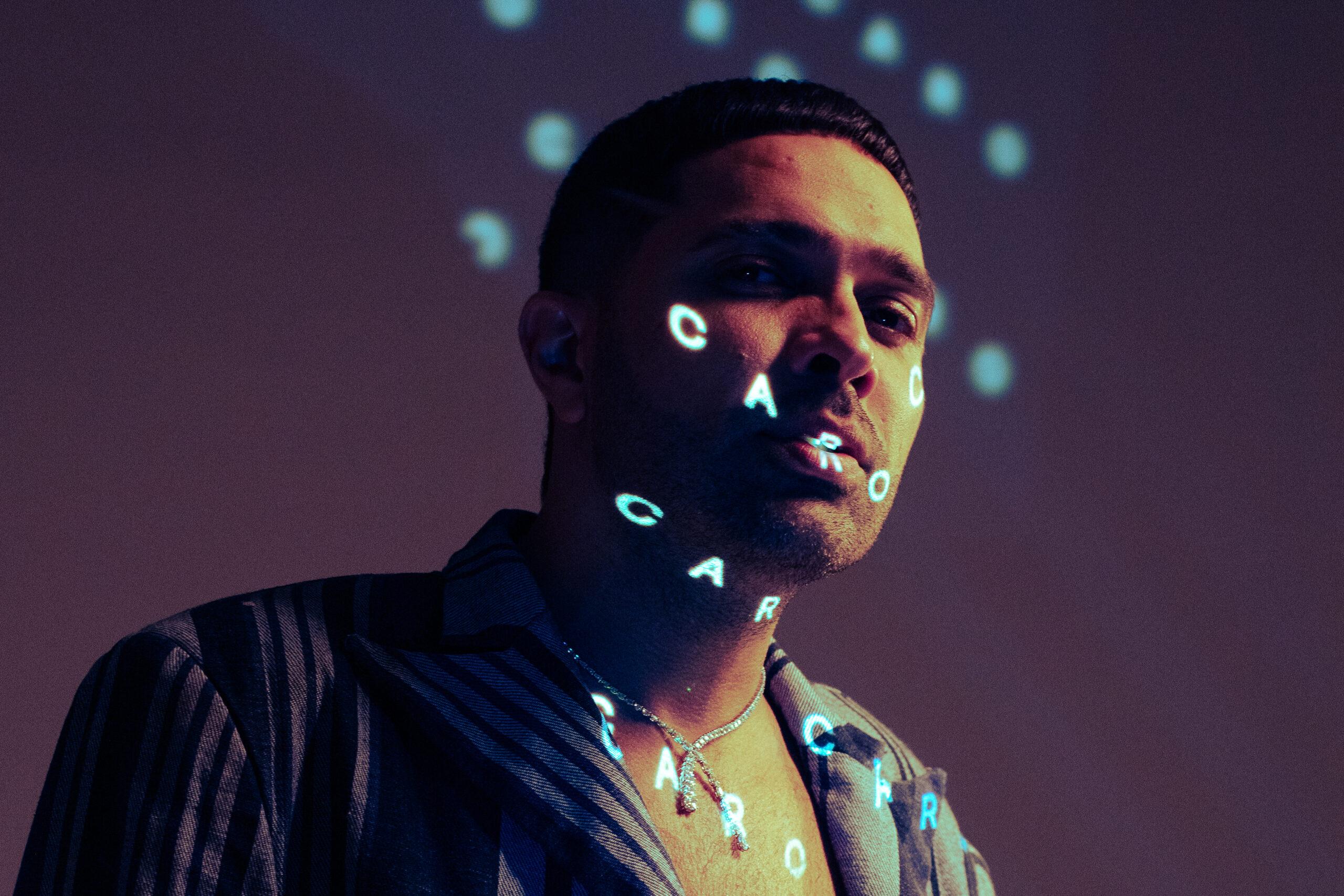 Na imagem vemos o o rapper em contra-luz com letras projectadas na sua face onde se lê "Caro Vapor"